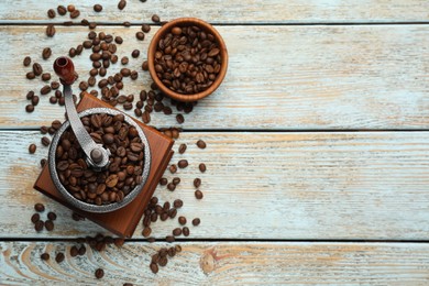 Photo of Vintage manual coffee grinder with beans on light wooden table, flat lay. Space for text