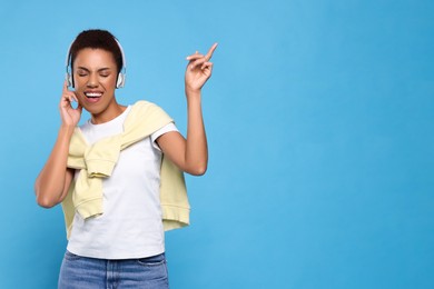 Photo of Happy young woman in headphones dancing on light blue background. Space for text