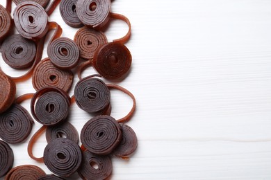 Photo of Delicious fruit leather rolls on white wooden table, flat lay. Space for text