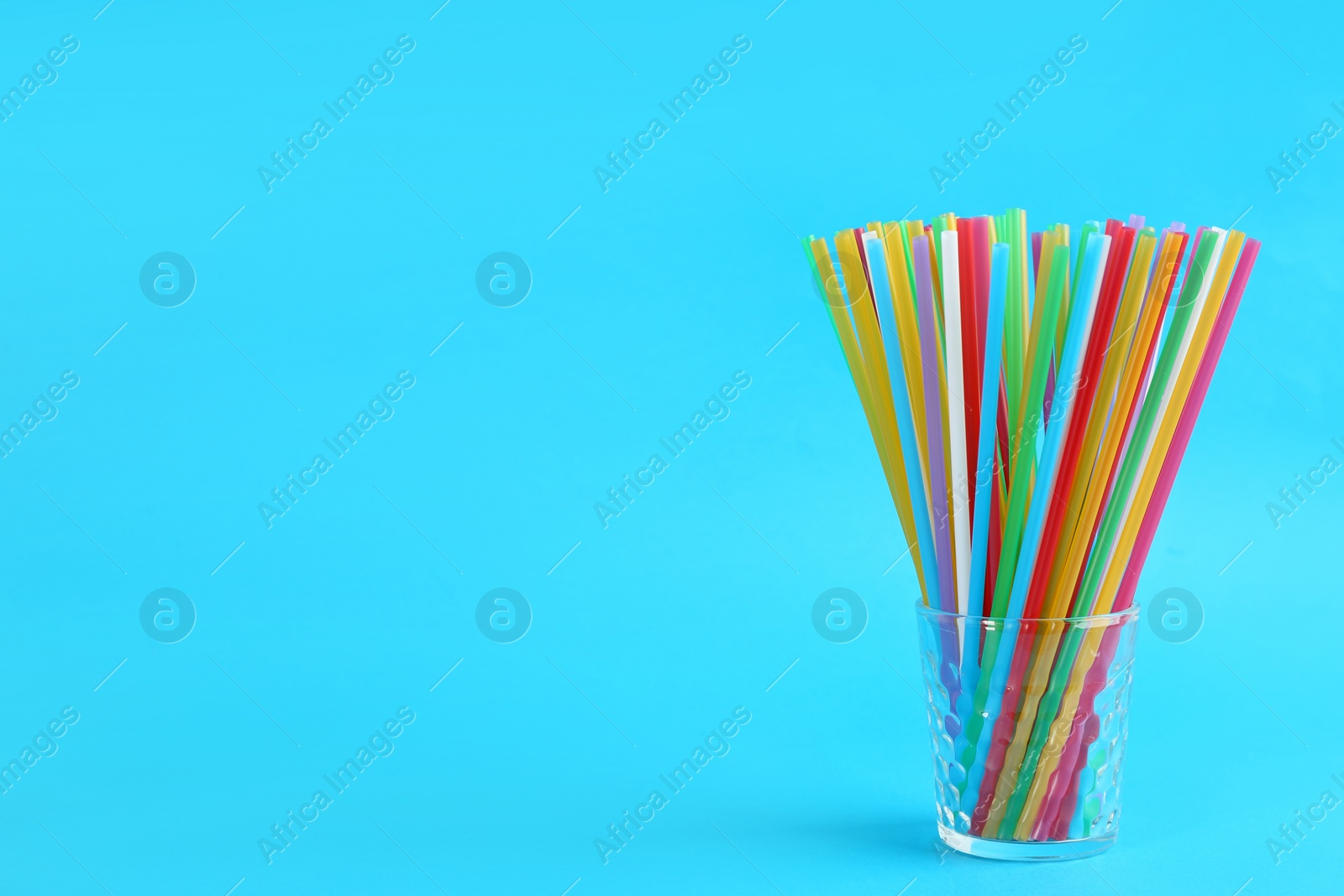 Photo of Colorful plastic drinking straws in glass on light blue background, space for text