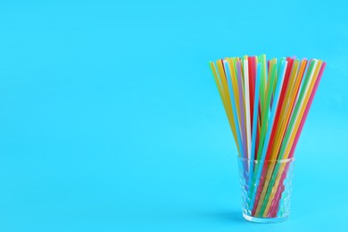 Photo of Colorful plastic drinking straws in glass on light blue background, space for text