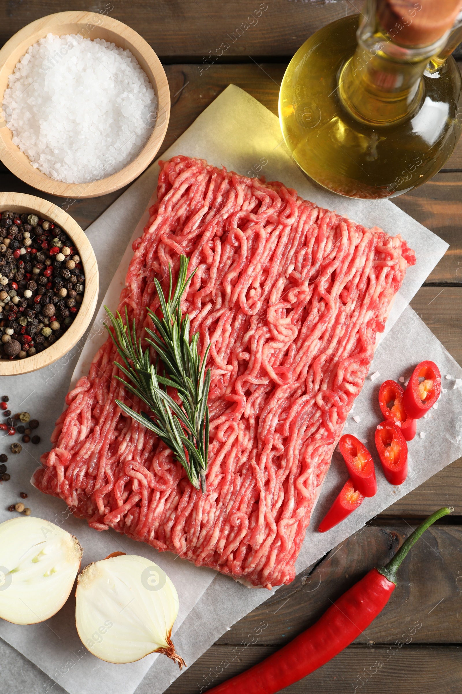 Photo of Raw ground meat, spices, rosemary, oil and onion on wooden table, flat lay