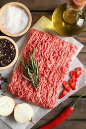 Raw ground meat, spices, rosemary, oil and onion on wooden table, flat lay