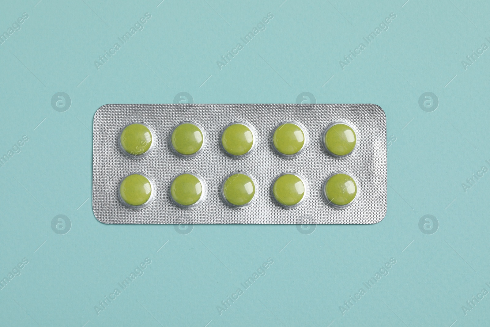 Photo of Green pills in blister on turquoise background, top view