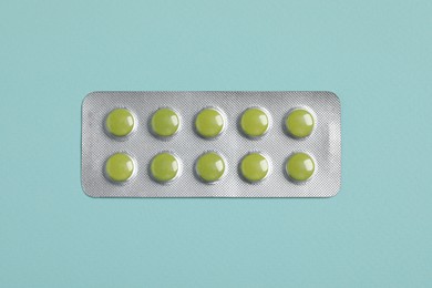 Photo of Green pills in blister on turquoise background, top view