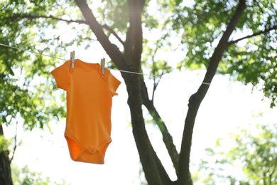 Photo of Color baby onesie hanging on clothes line outside. Space for text