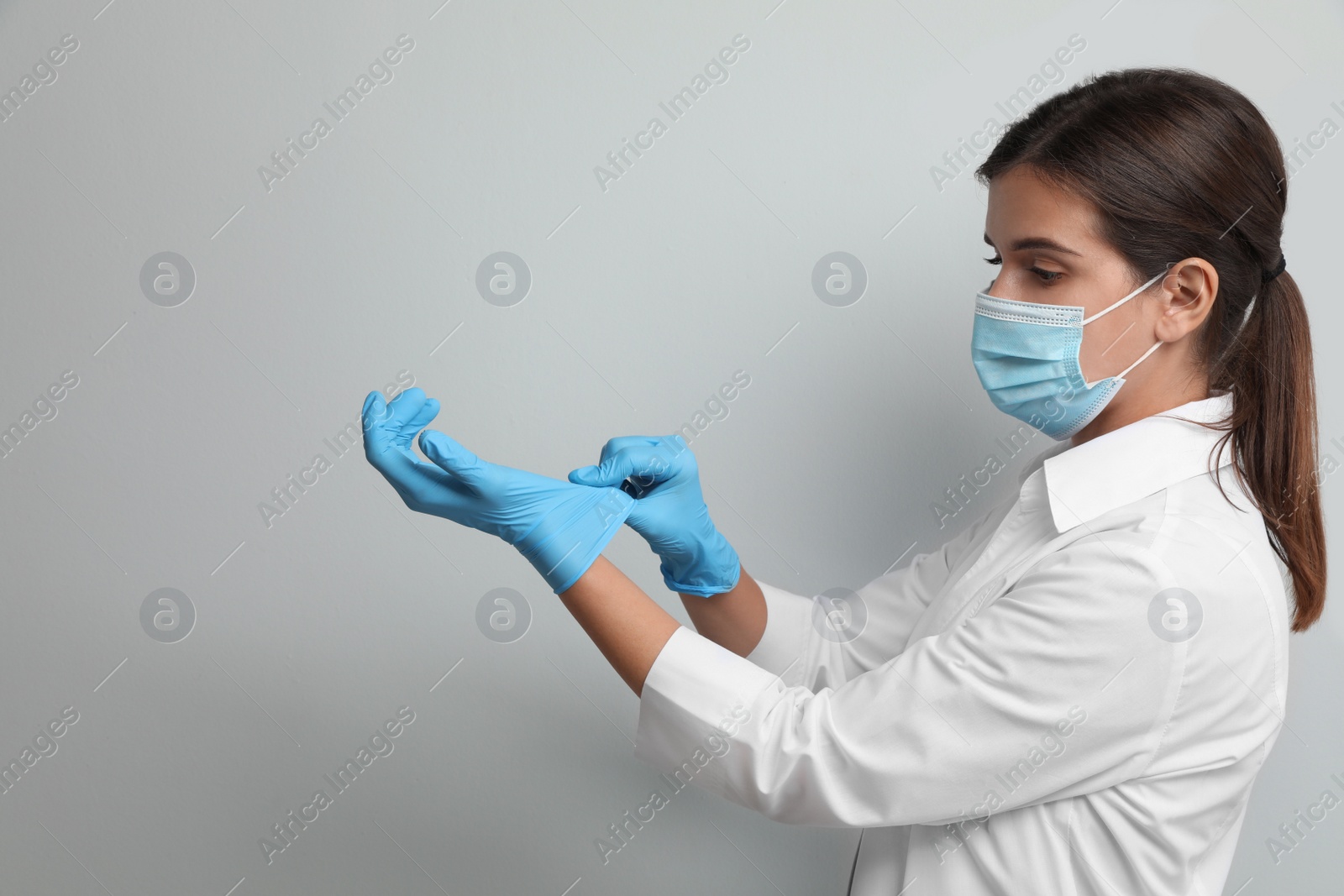 Photo of Doctor in protective mask putting on medical gloves against light grey background