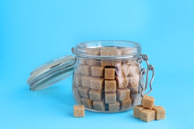 Photo of Brown sugar cubes in glass jar on light blue background