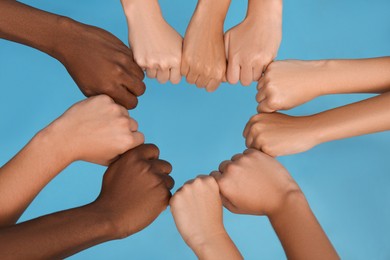 Photo of Group of multiracial people joining fists together on light blue background, closeup