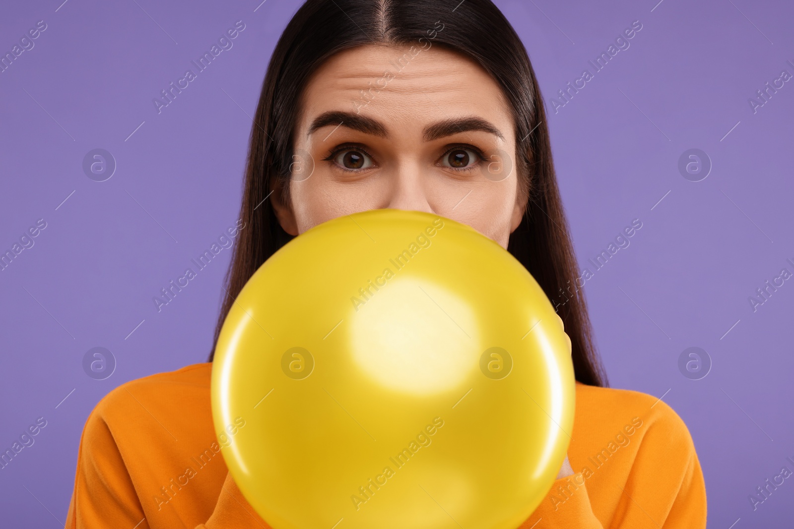 Photo of Woman inflating yellow balloon on purple background