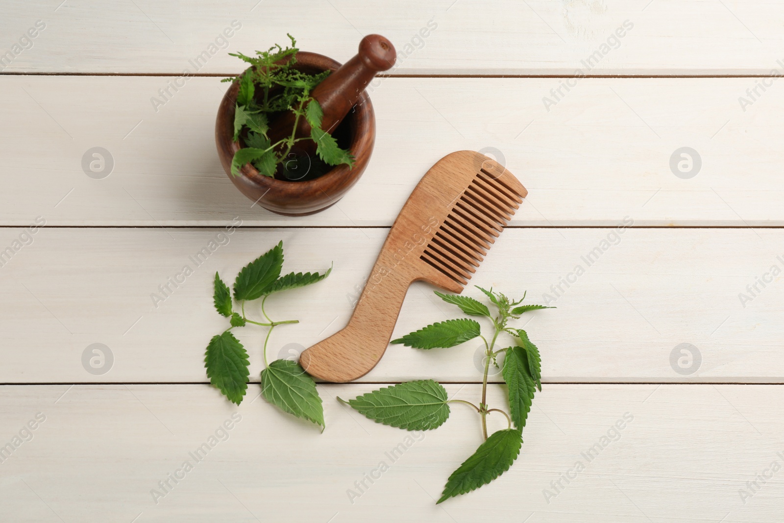 Photo of Stinging nettle and comb on white wooden background, flat lay. Natural hair care