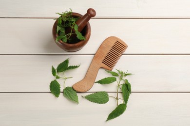 Photo of Stinging nettle and comb on white wooden background, flat lay. Natural hair care