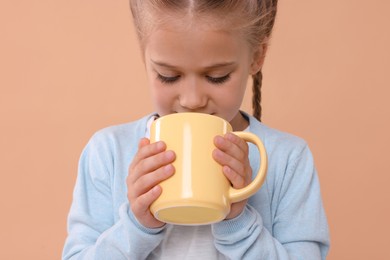 Photo of Cute girl drinking beverage from yellow ceramic mug on beige background