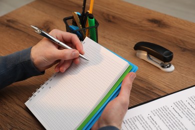 Photo of Man taking notes at wooden table, closeup