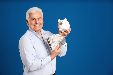 Photo of Happy senior man with cash money and piggybank on blue background. Space for text