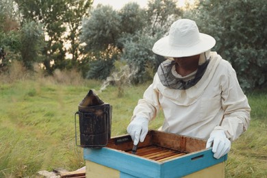 Beekeeper scraping wax from honey frame at apiary