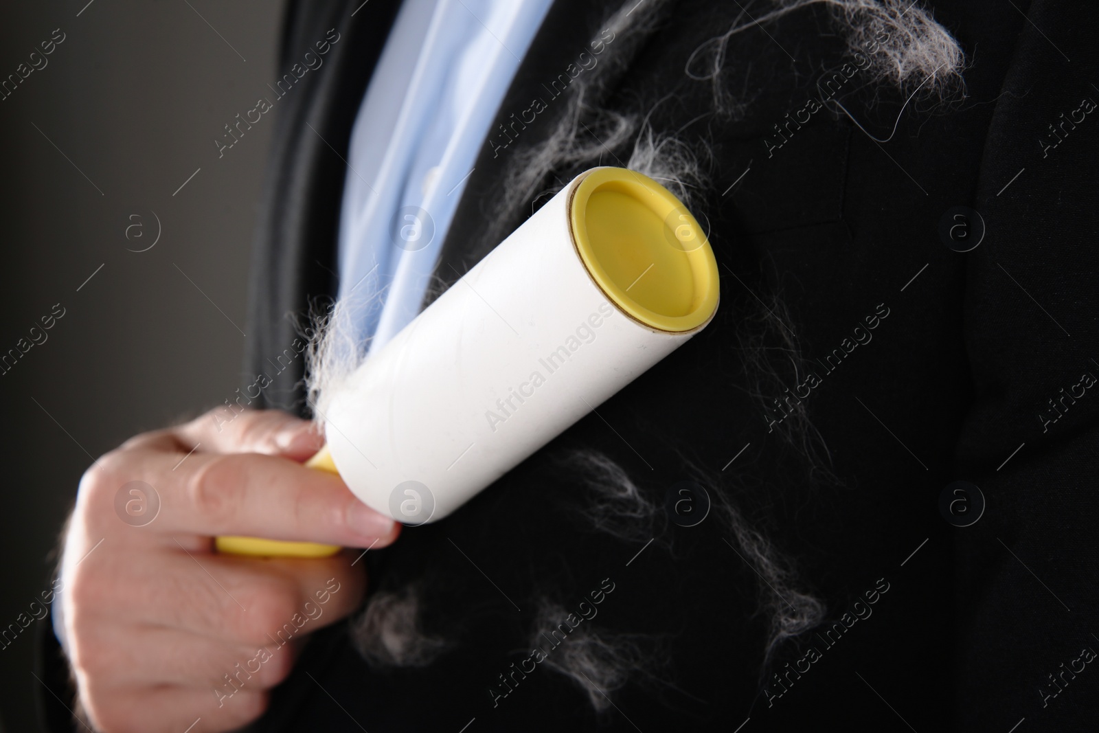 Photo of Man removing hair from black jacket with lint roller on grey background, closeup