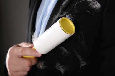 Man removing hair from black jacket with lint roller on grey background, closeup