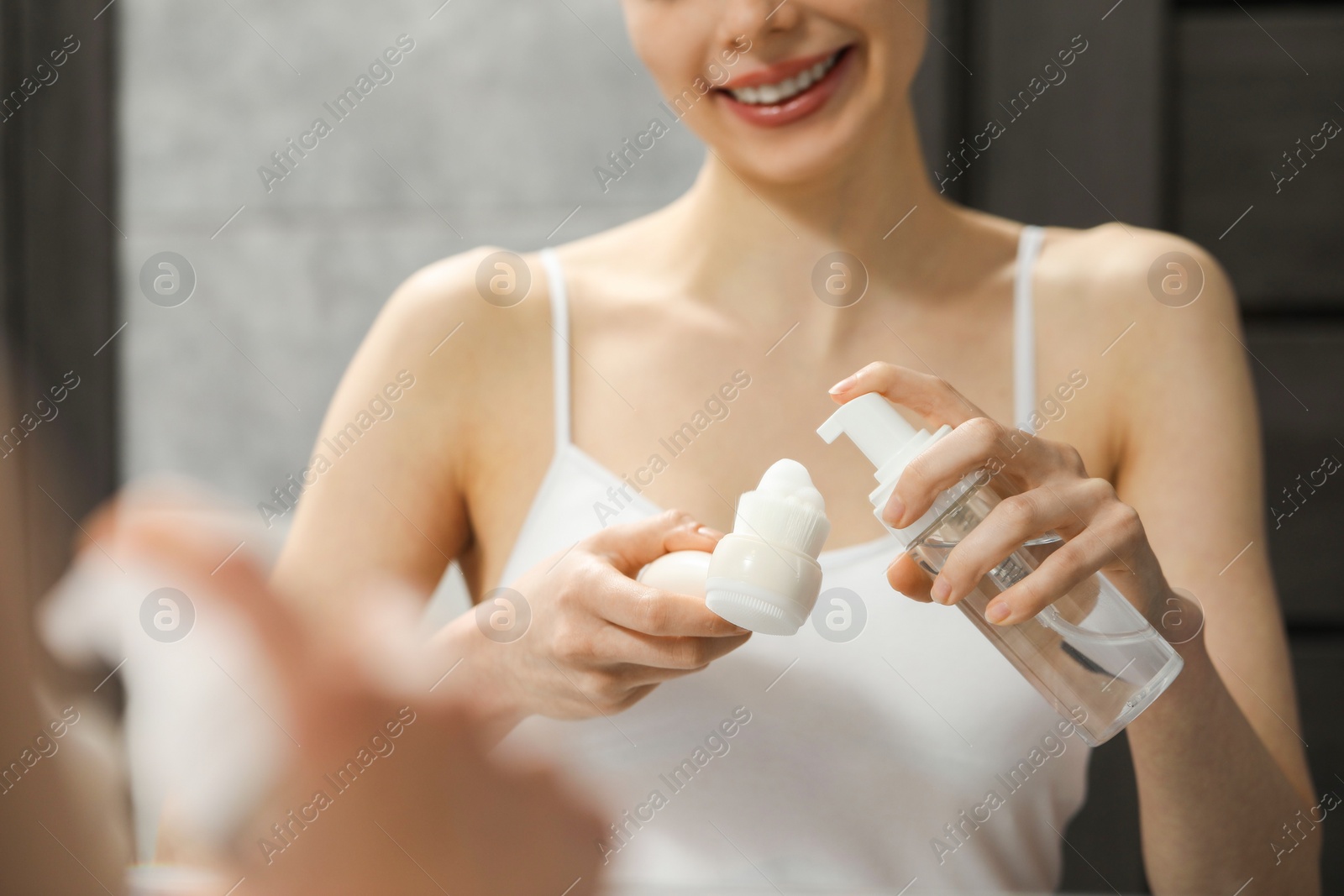 Photo of Washing face. Woman applying cleansing foam onto brush near mirror in bathroom, closeup