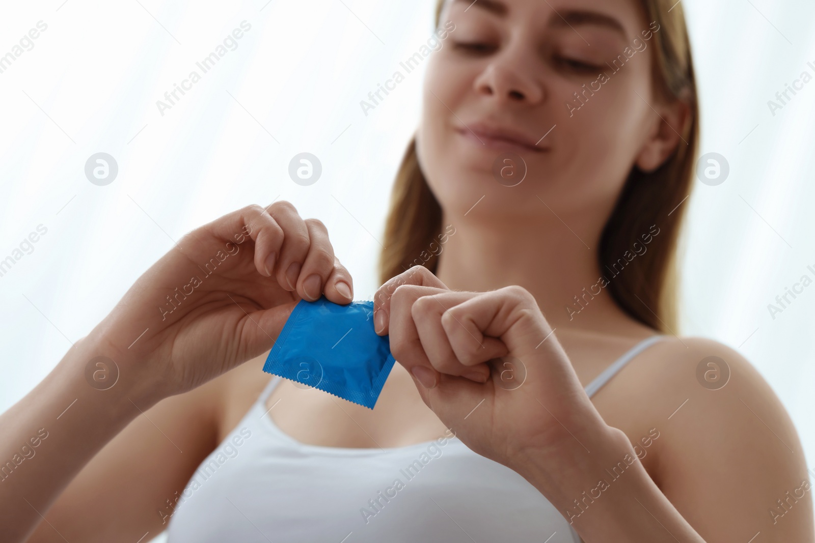 Photo of Woman opening condom indoors, selective focus. Safe sex