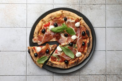 Photo of Tasty pizza with cured ham, olives, mozzarella cheese, sun-dried tomato and basil on light tiled table, top view