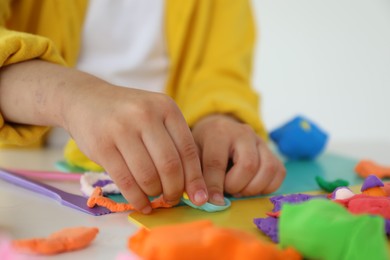 Photo of Little girl sculpting with play dough at white table indoors, closeup