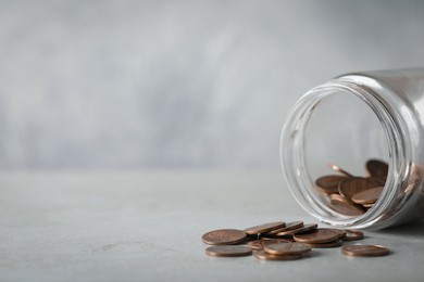 Glass jar with coins on light grey table, closeup. Space for text