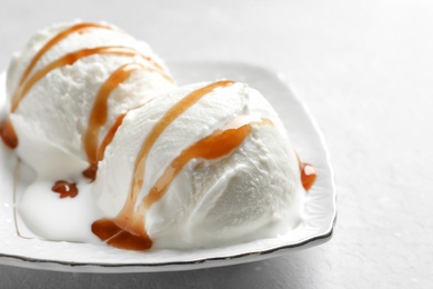 Photo of Tasty ice cream with caramel sauce on plate on table, closeup