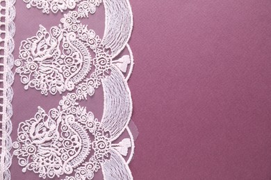 Photo of White lace on purple background, top view. Space for text