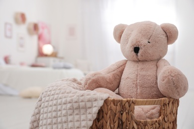 Photo of Cute teddy bear and blanket in wicker basket indoors