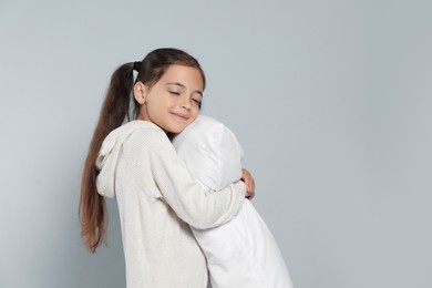 Photo of Cute girl in white pajamas hugging pillow on light grey background. Space for text