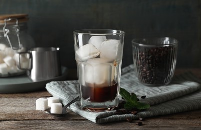 Photo of Glass of ice cubes with coffee, mint and sugar on wooden table