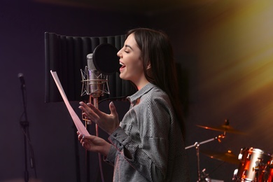 Photo of Young singer with microphone recording song in studio