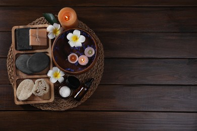 Different spa products, plumeria flowers and burning candles on wooden table, top view. Space for text