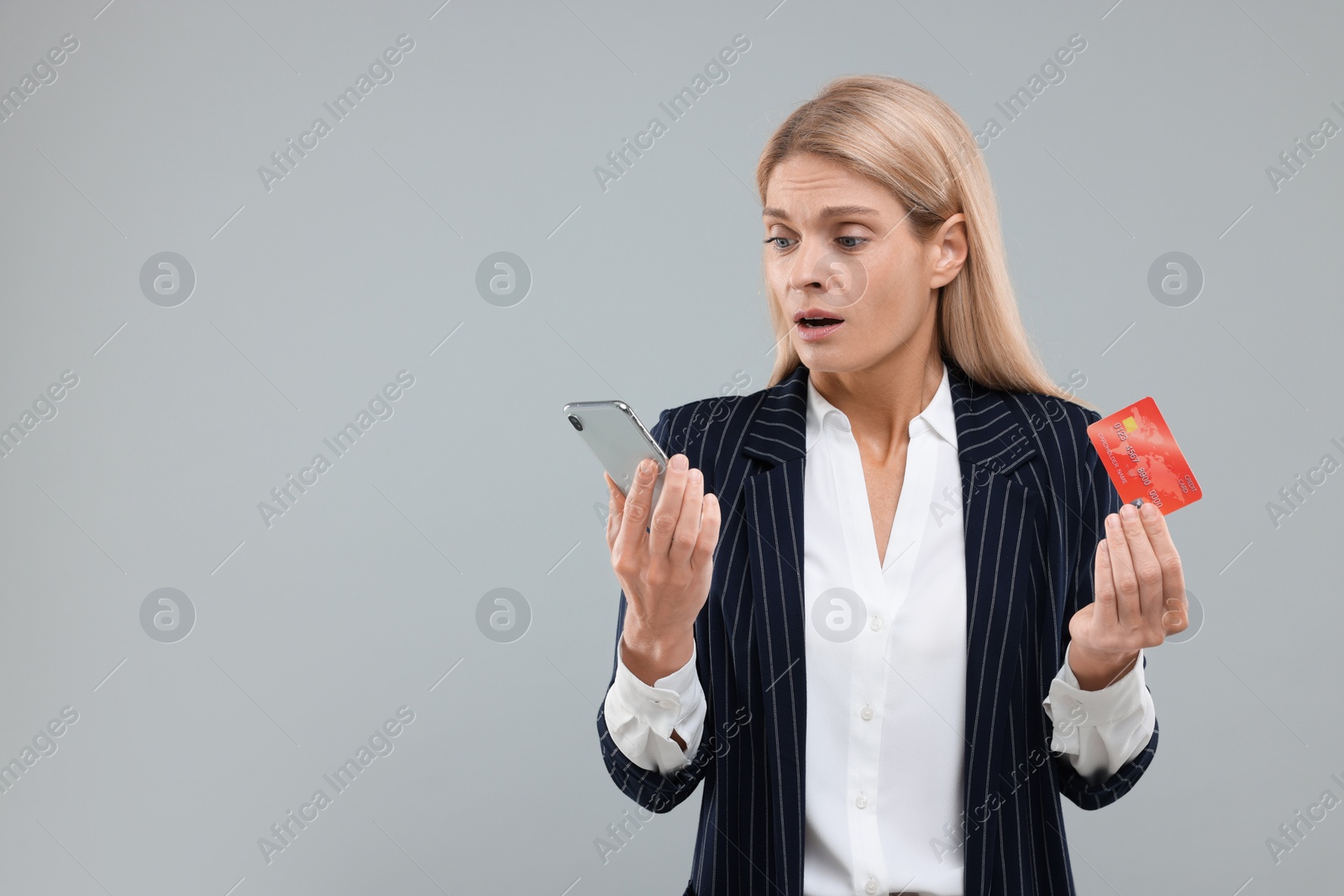 Photo of Stressed woman with credit card and smartphone on grey background, space for text. Be careful - fraud