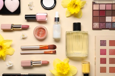 Photo of Flat lay composition with different makeup products and beautiful spring flowers on beige background