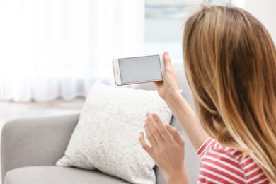 Photo of Young woman using video chat on smartphone in living room, closeup. Space for design