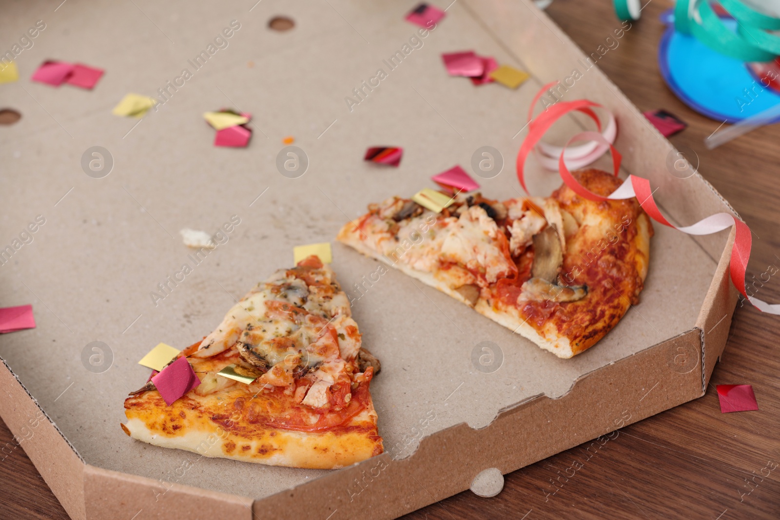 Photo of Pizza box with leftovers and confetti on table, closeup. After party chaos