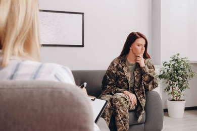 Sad female military officer sitting on sofa in psychologist office