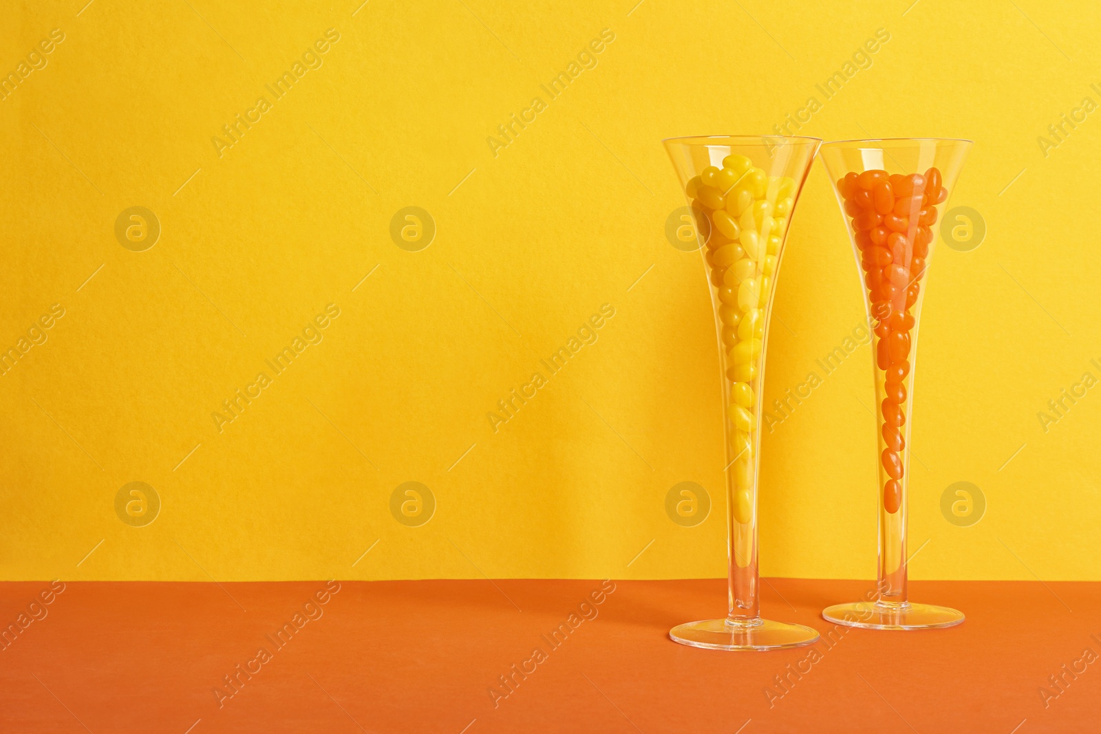 Photo of Glasses of tasty jelly beans on color background, space for text