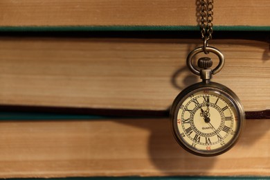 Photo of Pocket clock hanging on stack of books, closeup. Space for text