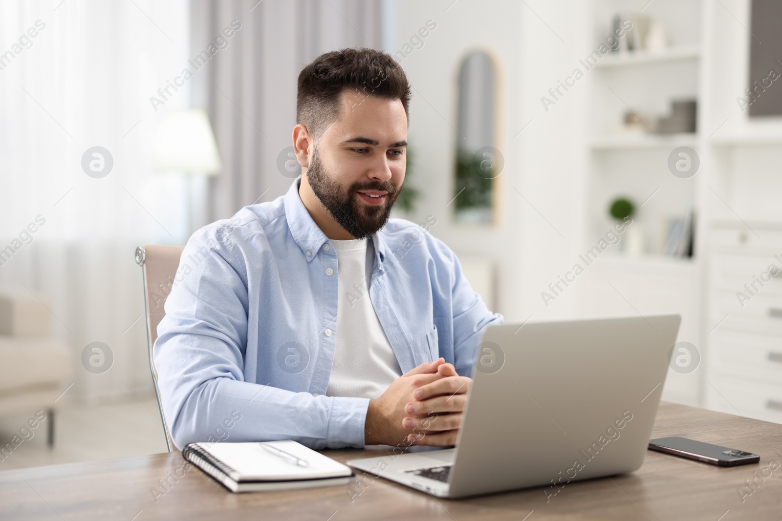 Photo of Young man watching webinar at table in room