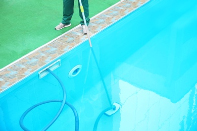 Photo of Male worker cleaning outdoor pool with underwater vacuum