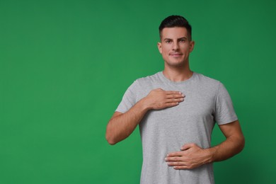 Photo of Handsome man holding hands near chest on green background. Space for text