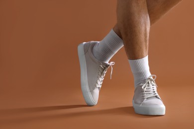 Photo of Man wearing stylish sneakers on brown background, closeup. Space for text