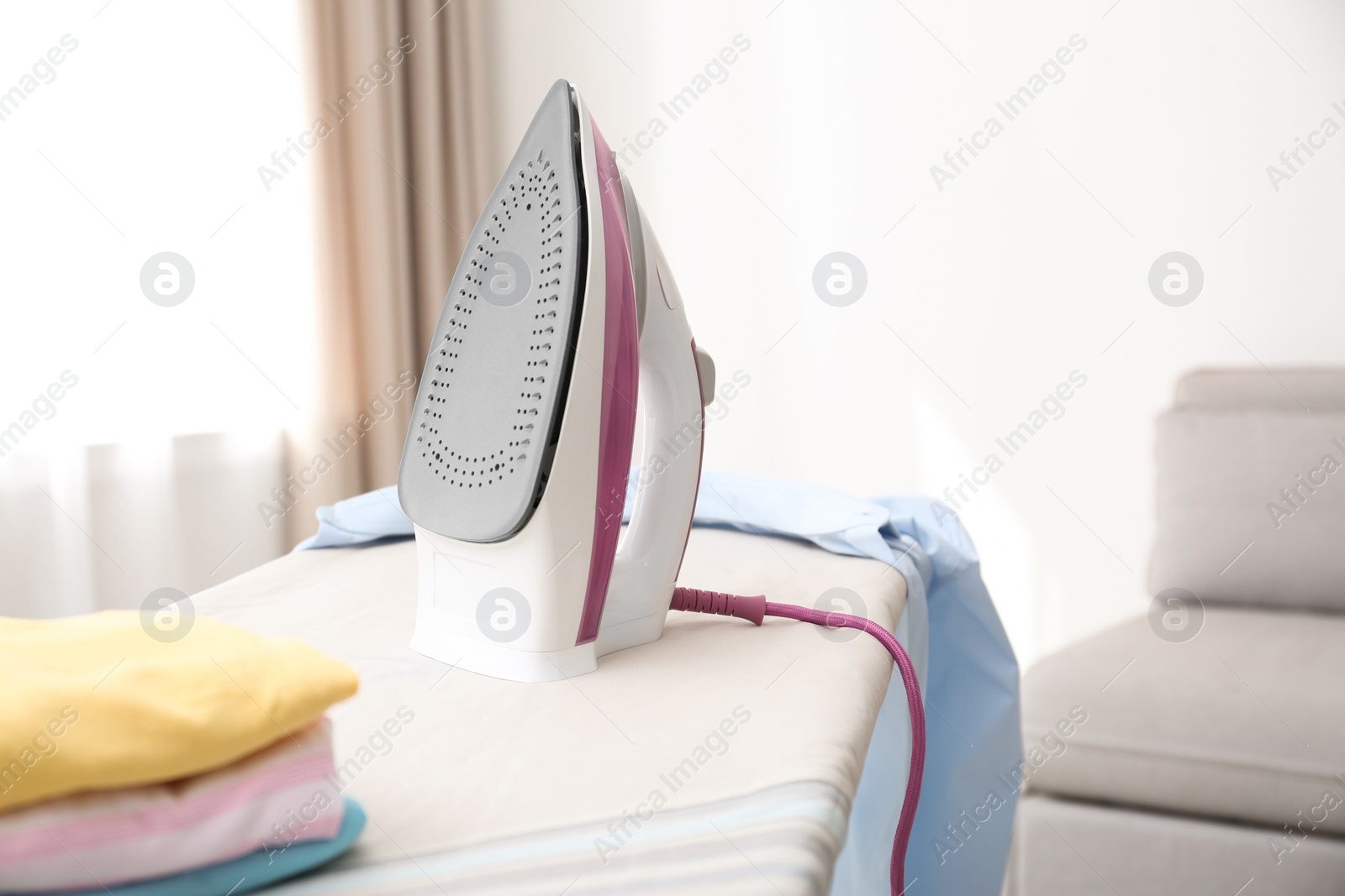 Photo of Board with modern iron and clean clothes indoors. Laundry day