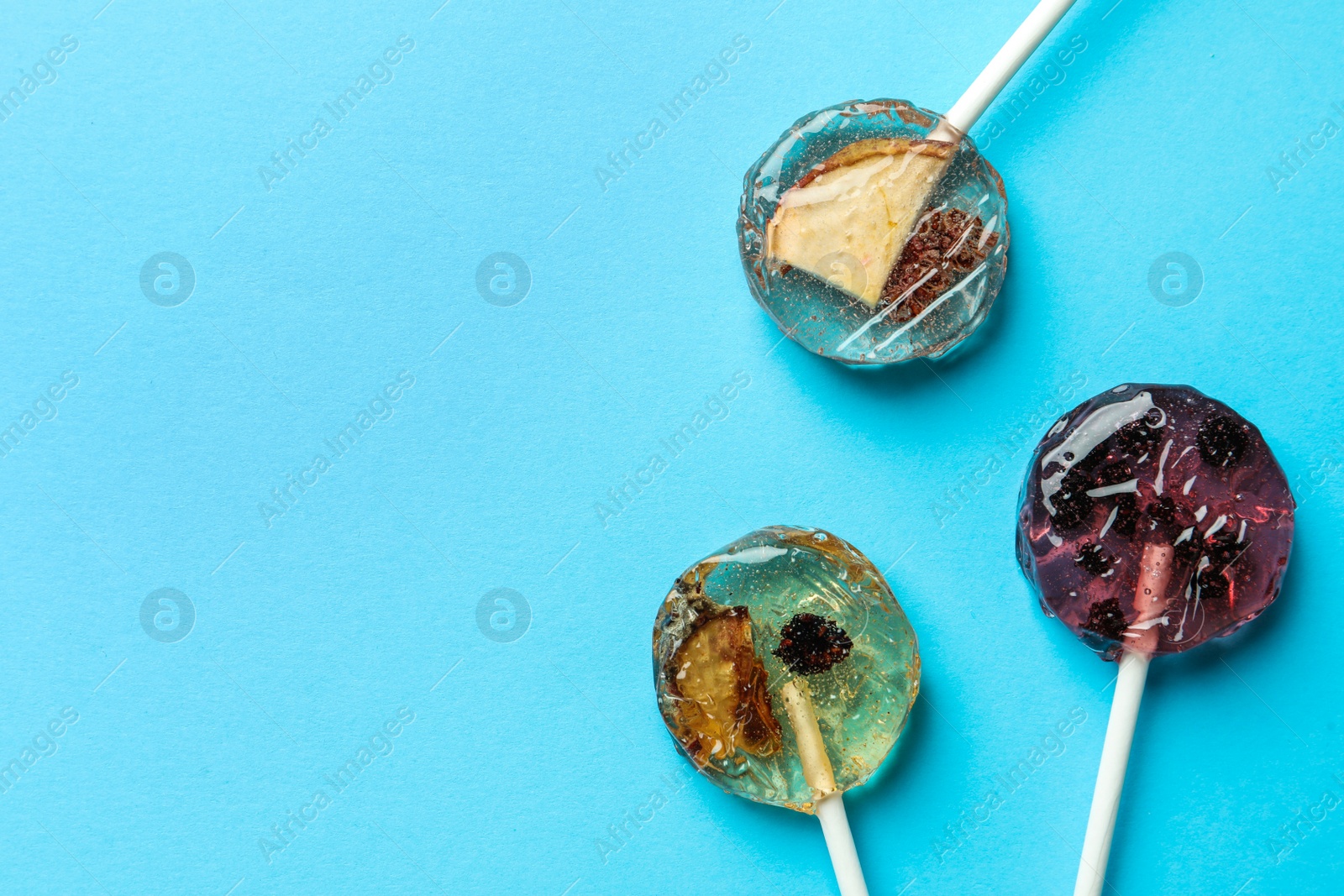 Photo of Sweet colorful lollipops with berries on light blue background, flat lay. Space for text