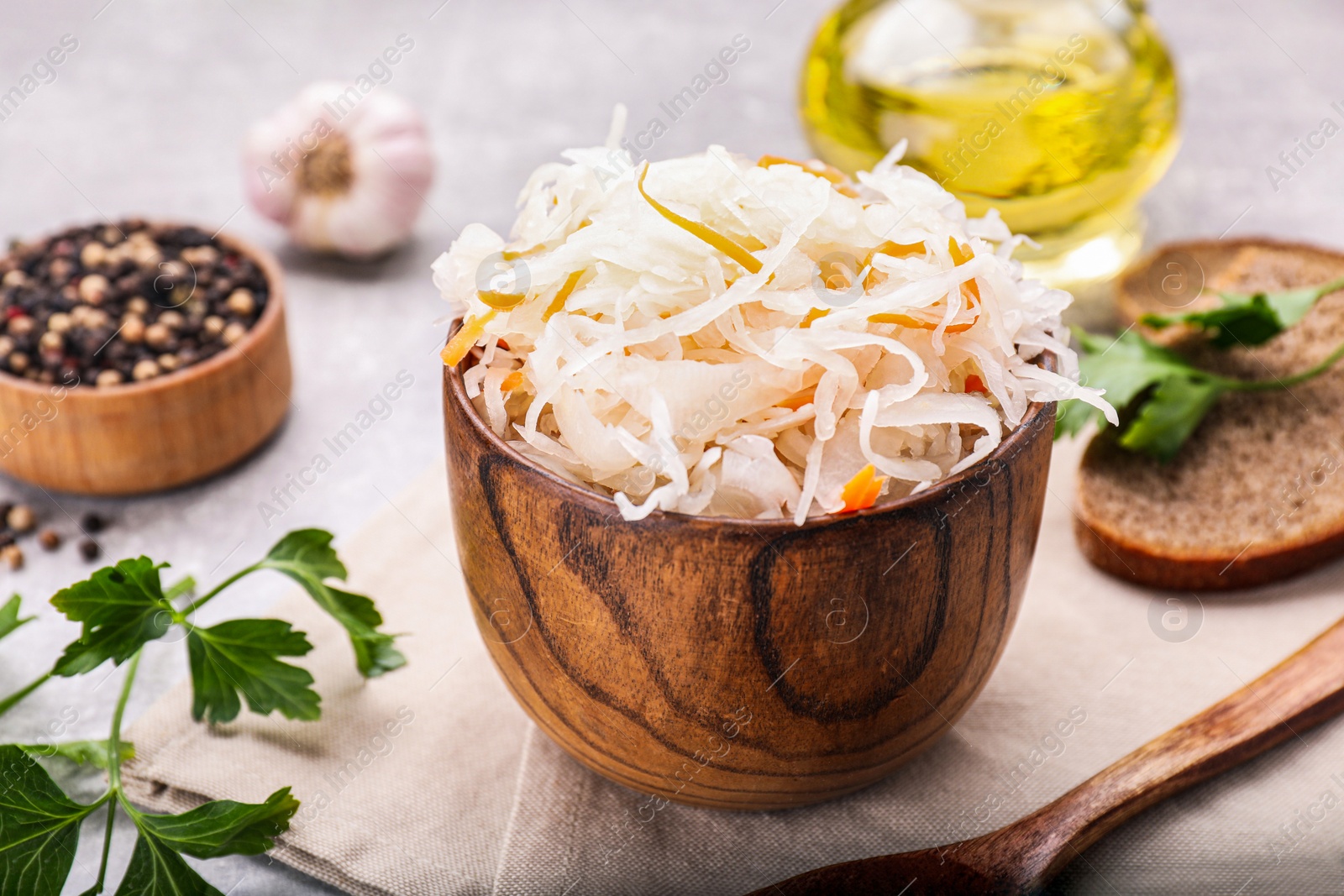 Photo of Bowl of tasty sauerkraut and ingredients on grey table, closeup