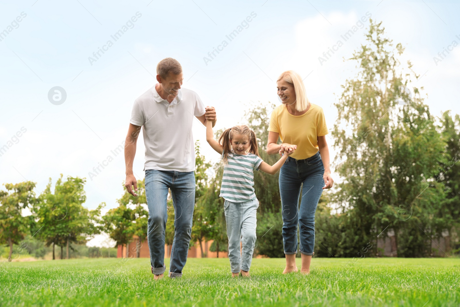 Photo of Cute little girl having fun with her parents in park on summer day