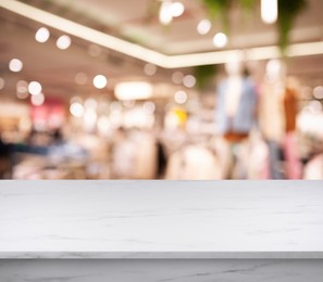 Image of Empty white marble surface and blurred view of clothes store interior. Space for design